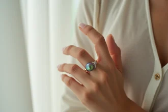 Bague de fiançailles avec perle de culture de Tahiti aux reflets paon sur le doigt d'une femme, gros plan macro